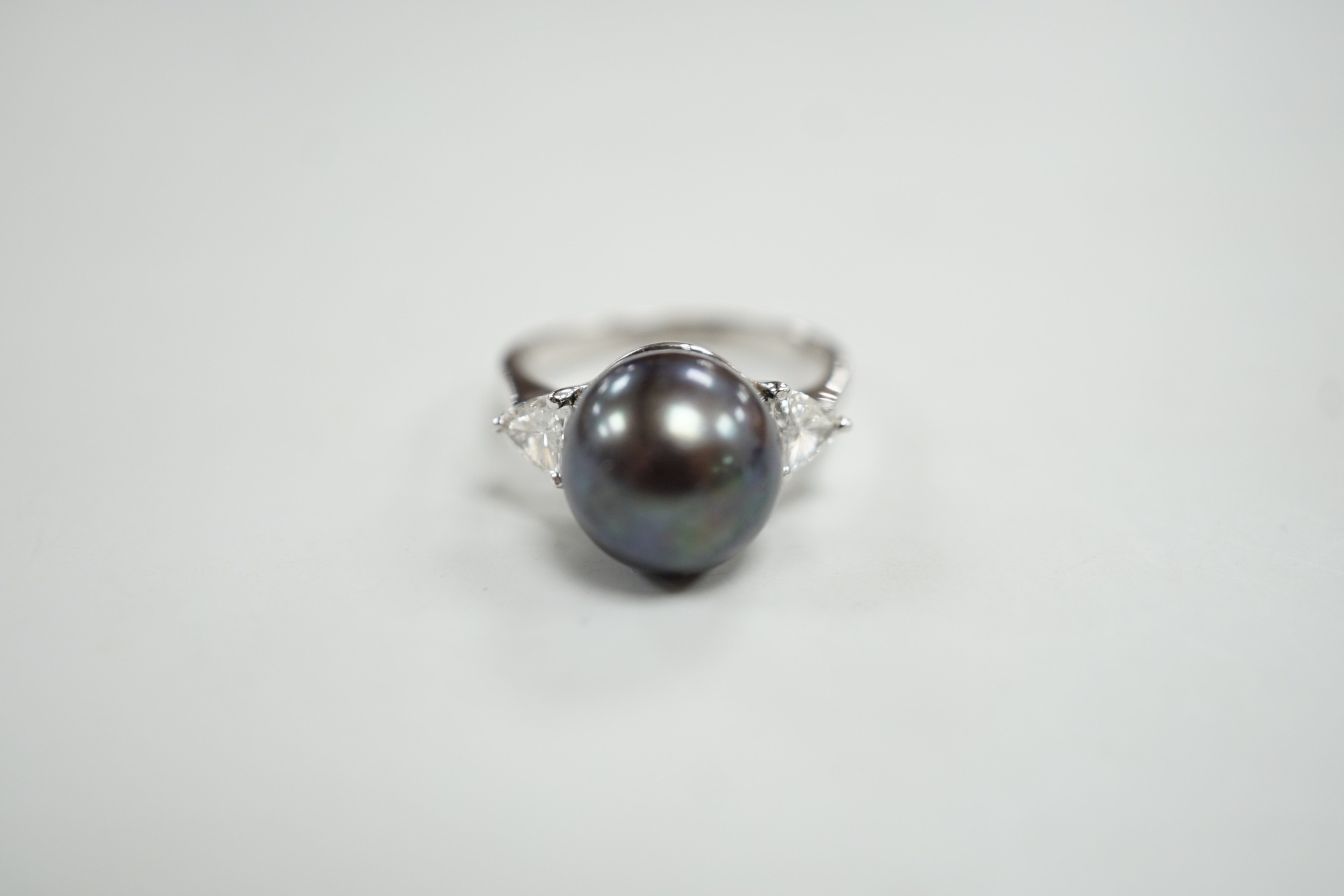 A modern 750 white metal, single stone Tahitian pearl and two stone trillion cut diamond set ring, size O, gross weight 5.6 grams.